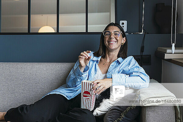 Glückliche Frau  die Popcorn isst und es auf dem Sofa im Wohnzimmer genießt