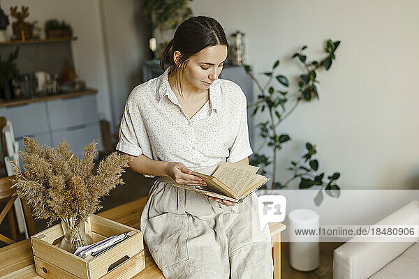 Frau liest Buch und sitzt zu Hause am Tisch