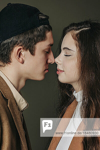 Loving teenage couple rubbing noses against gray background