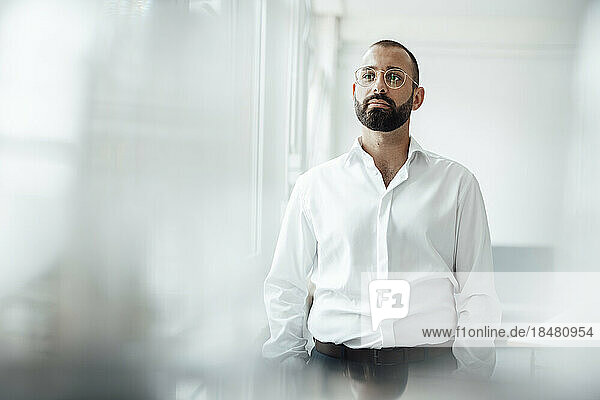 Contemplative businessman wearing eyeglasses standing at home office