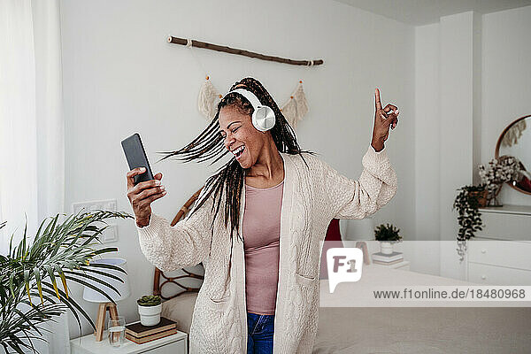Cheerful woman wearing wireless headphones dancing in bedroom at home