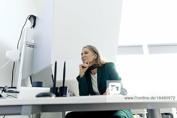Senior businesswoman with hand on chin sitting at desk in office