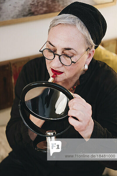 Woman applying red lipstick looking in mirror at home