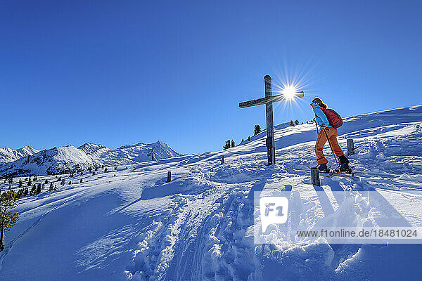 Austria  Tyrol  Female skier passing Christian cross in Zillertal Alps