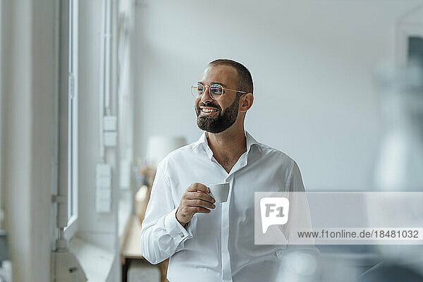 Happy businessman with cup of coffee standing at home office