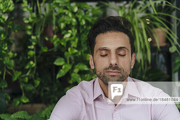 Mature businessman with eyes closed in front of plants