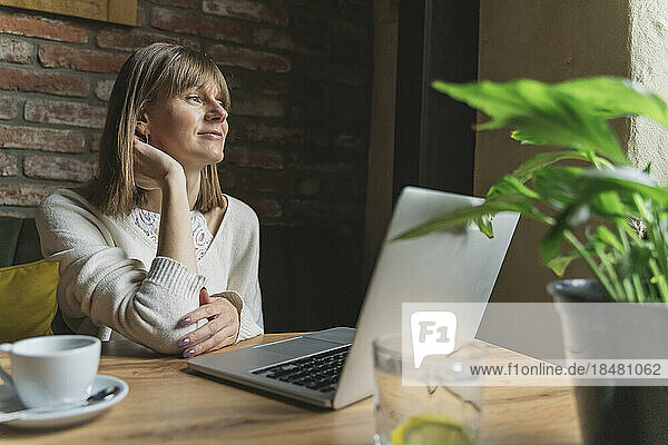 Thoughtful freelancer with laptop sitting at table in cafe