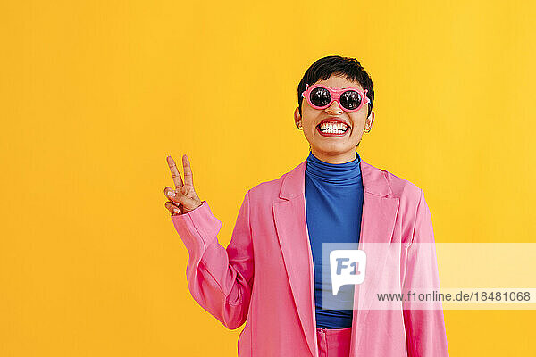 Playful young woman wearing sunglasses gesturing against colored background
