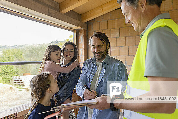Reifer Mann mit Familie unterschreibt Dokument auf der Baustelle