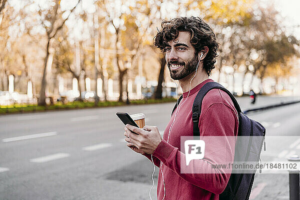 Smiling man with smart phone standing at sidewalk