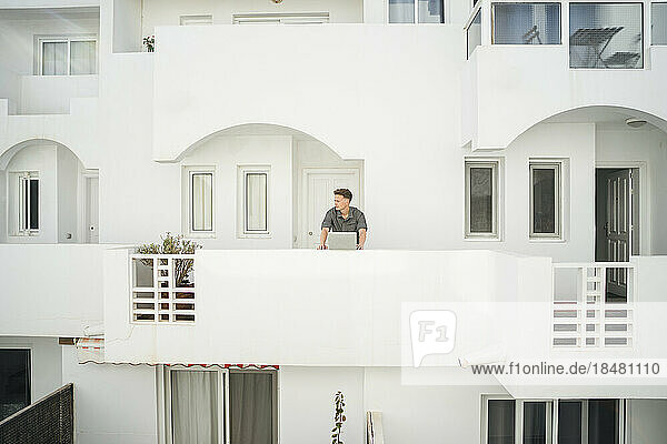Man standing with laptop in balcony