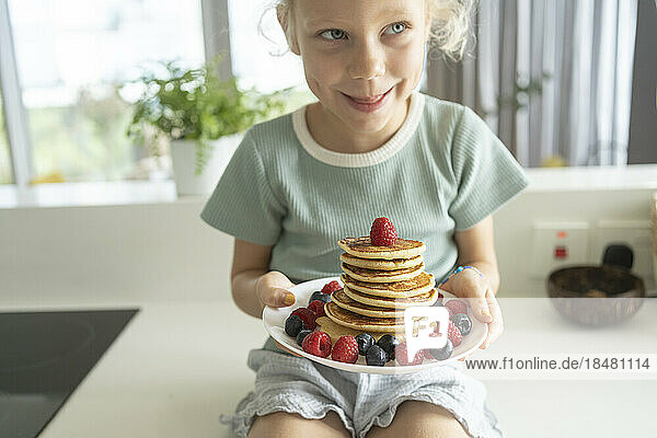 Girl holding stack of pancakes with berries in kitchen