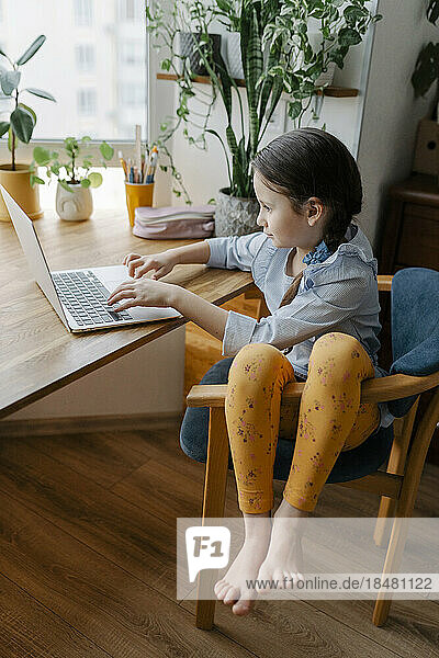Girl using laptop sitting at table in home