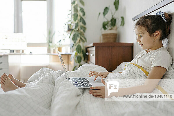 Cute girl using laptop on bed in bedroom