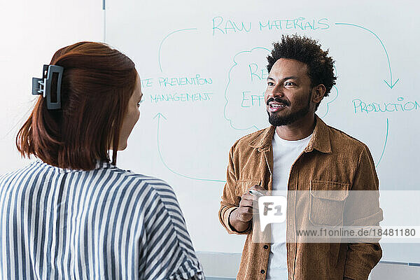 Smiling businessman having discussion with colleague in front of whiteboard