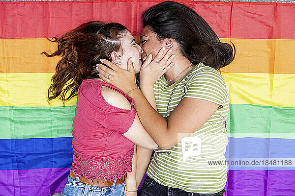 Glückliche Frau küsst Freundin  die auf Regenbogenfahne liegt