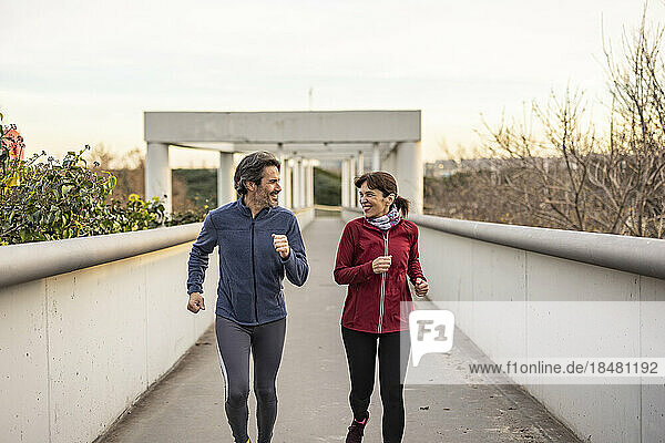 Happy mature couple jogging on bridge