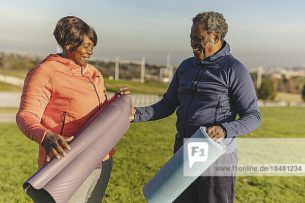 Happy senior woman folding exercise mat with man in park