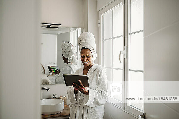 Glückliche reife Frau benutzt Tablet-PC im Badezimmer zu Hause
