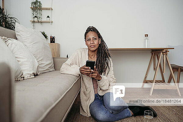 Freelancer sitting with smart phone by sofa at home office