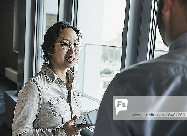 Businesswoman wearing eyeglasses discussing with colleague near window at office