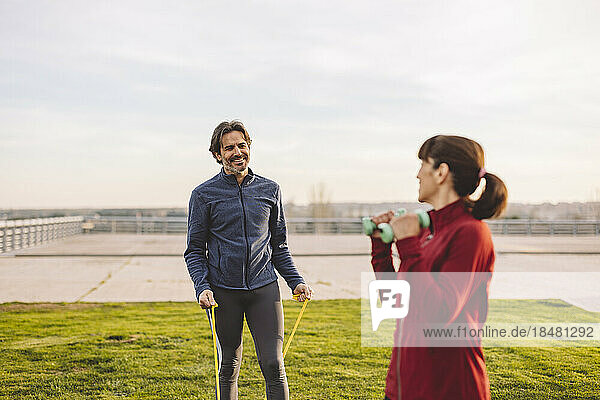 Happy man exercising with woman in park on sunny day