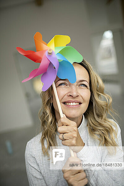 Smiling woman holding multi colored pinwheel toy near face