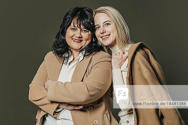 Happy mother and daughter wearing brown coat against gray background