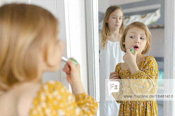 Girl applying lipstick looking in mirror at home
