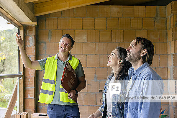 Lächelnder Bauunternehmer diskutiert mit älterem Paar auf der Baustelle