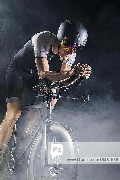 Cyclist practicing cycling on turbo trainer amidst smoke