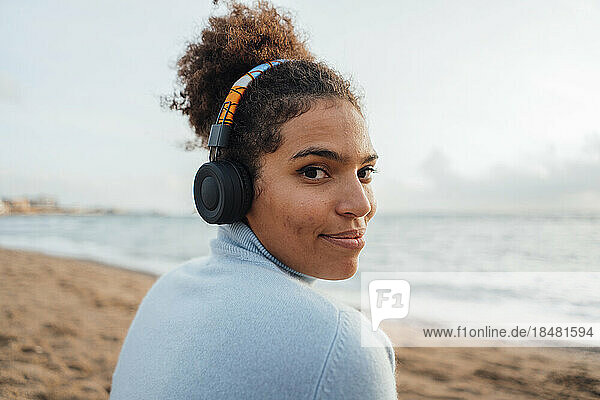 Smiling young woman wearing headphones listening to music at beach