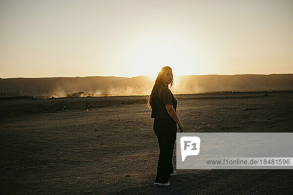 Young woman walking on dirt road at sunset