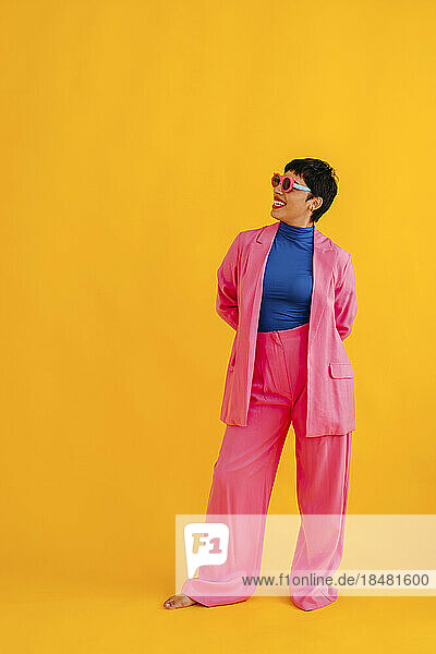 Smiling young woman wearing sunglasses standing against colored background