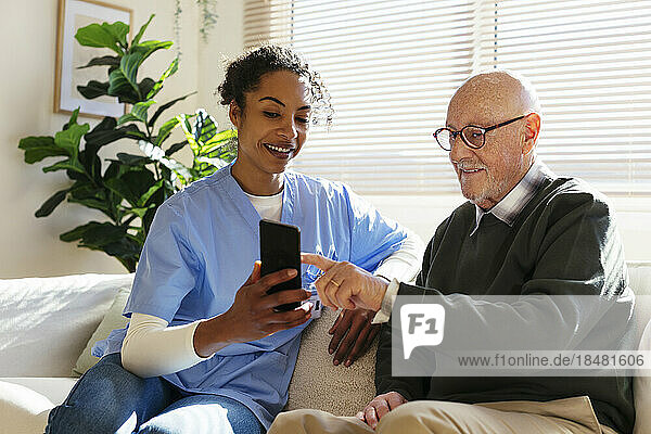 Smiling senior man sharing smart phone with caretaker at home