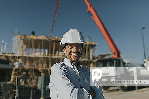 Happy mature architect wearing hardhat at construction site