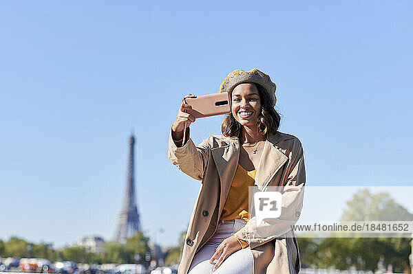 Happy young woman taking selfie through smart phone over blue sky