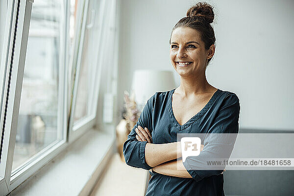 Smiling freelancer with arms crossed standing by window at home office