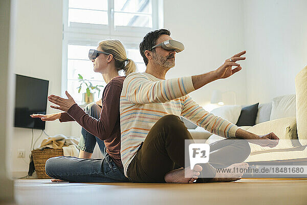 Mature couple wearing wearing virtual reality headset and gesturing at home