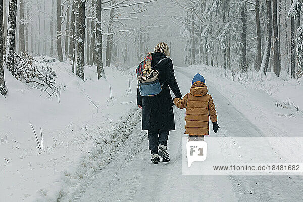Mother and son walking on footpath amidst snowy forest