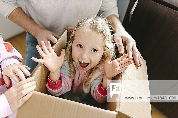 Happy girl sitting in cardboard box with sister and father at home