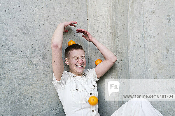 Fröhliche nicht-binäre Person  die Spaß mit Orangen vor der Wand hat