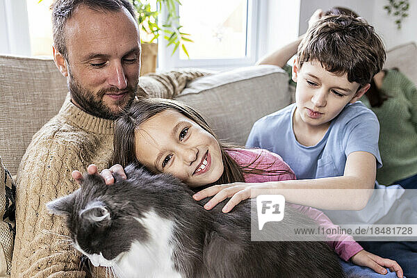 Glücklicher Vater mit Tochter und Sohn  die zu Hause auf dem Sofa eine Katze streicheln