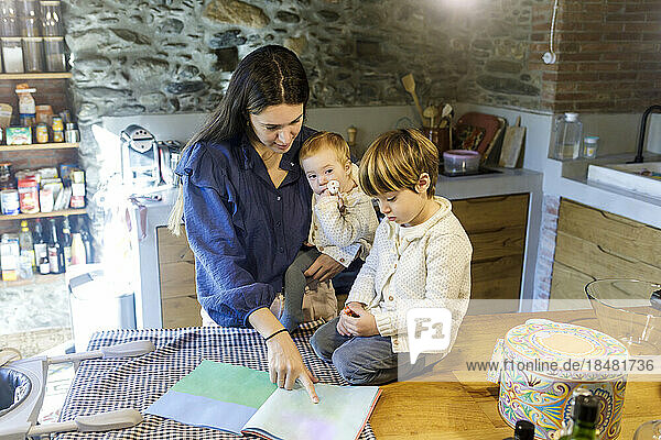 Mother with children reading picture book in kitchen