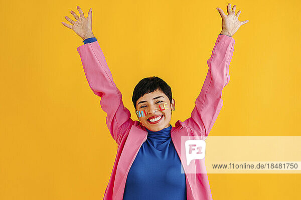 Happy young woman with arms raised standing over colored background