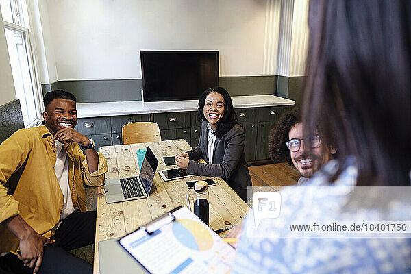 Zufriedene Geschäftskollegen sitzen bei einer Bürobesprechung am Schreibtisch