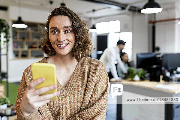 Happy businesswoman with smart phone standing in office