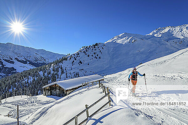 Austria  Tyrol  Sun shining over female skier walking past secluded hut in Tux Alps
