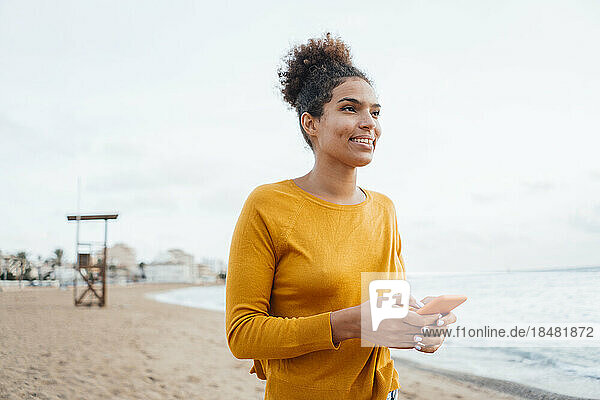 Thoughtful young woman with smart phone standing at beach