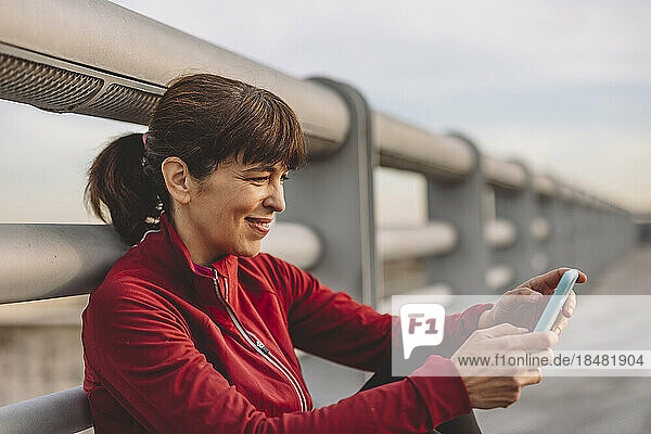 Happy mature woman using smart phone leaning on railing